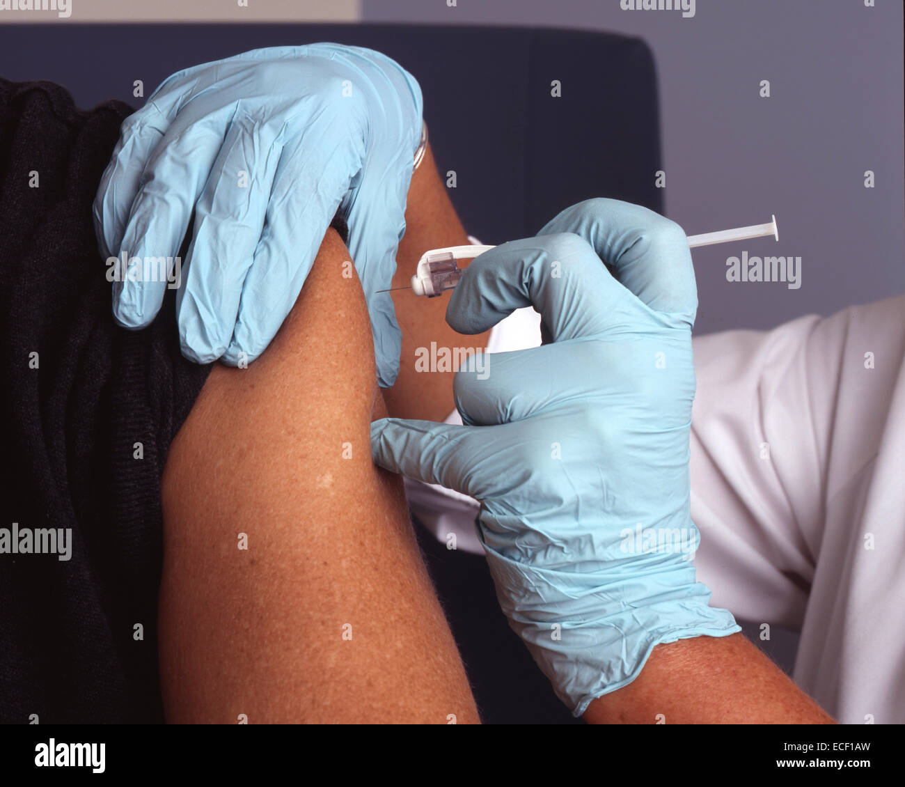 A nurse wearing blue gloves administers a vaccine (vaccination) into a male patient's arm. Stock Photo