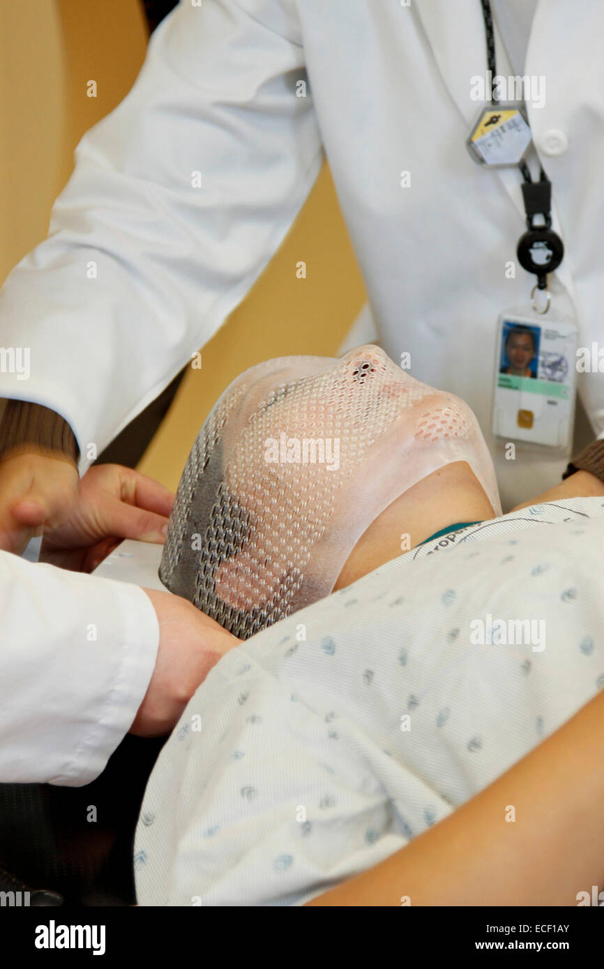 Two radiation therapists fit a short face mask to a patient model to steady the head during radiation therapy. Stock Photo