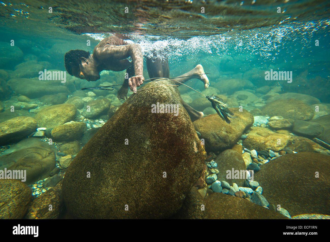 Agta man searching for fish in the clear tropical water of the Blos River Stock Photo