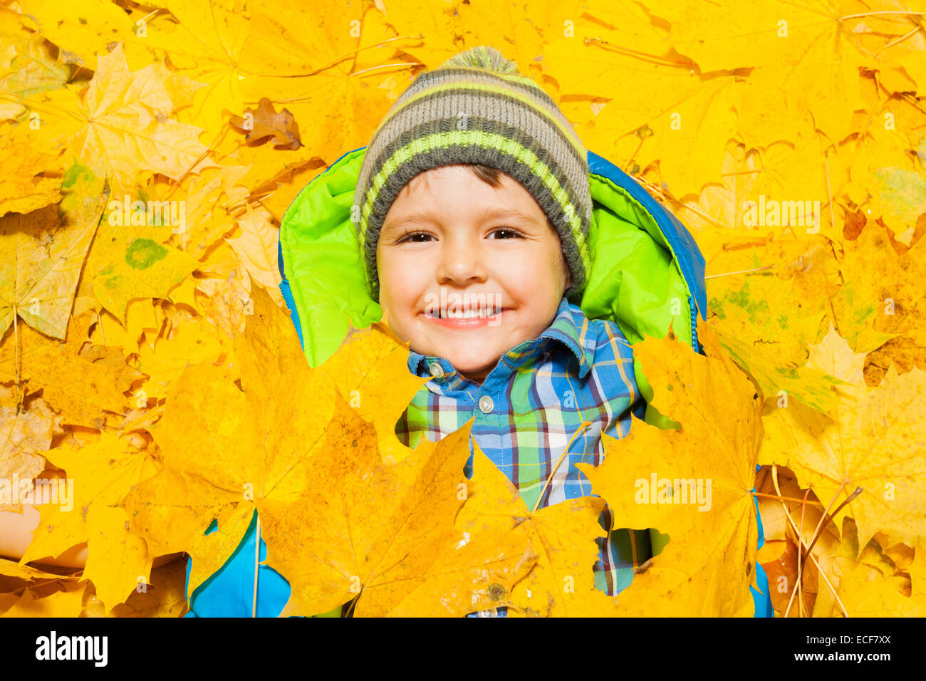 Happy little four years old boy laying in the yellow autumn leaves, smiling and covered with some of them Stock Photo