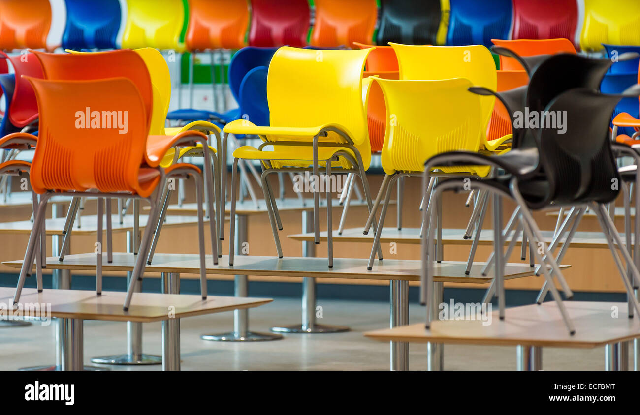 Brightly coloured plastic canteen chairs sitting on tables as if the floors  are to be cleaned Stock Photo - Alamy