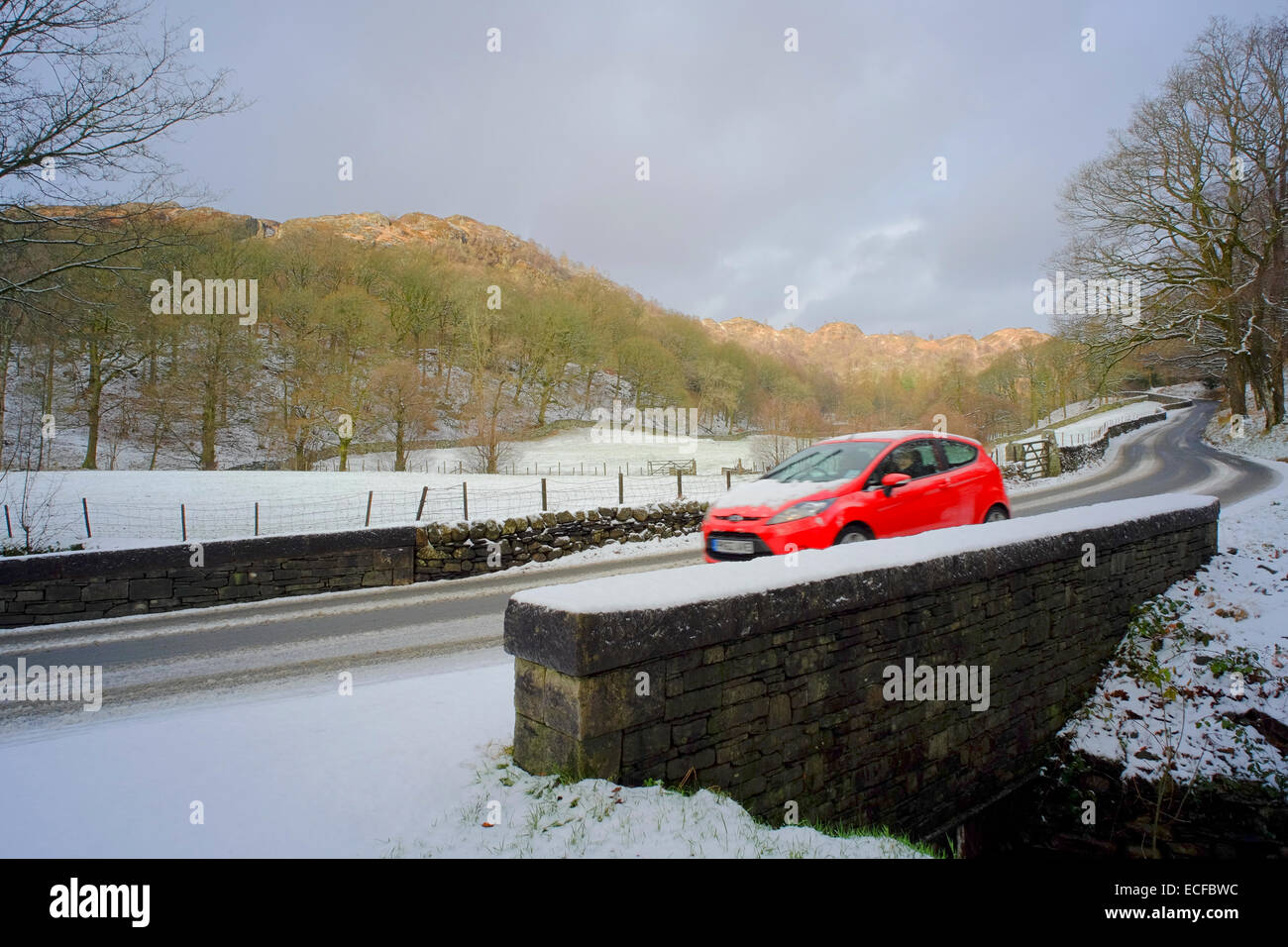 Red Car driving in snow in the Lake District Stock Photo