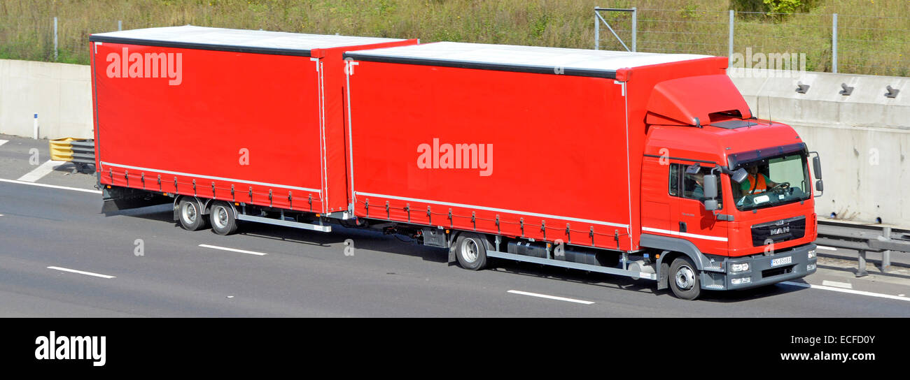 Driver in left hand drive foreign clean unmarked MAN lorry towing trailer driving along motorway red access curtain soft sided England UK Stock Photo