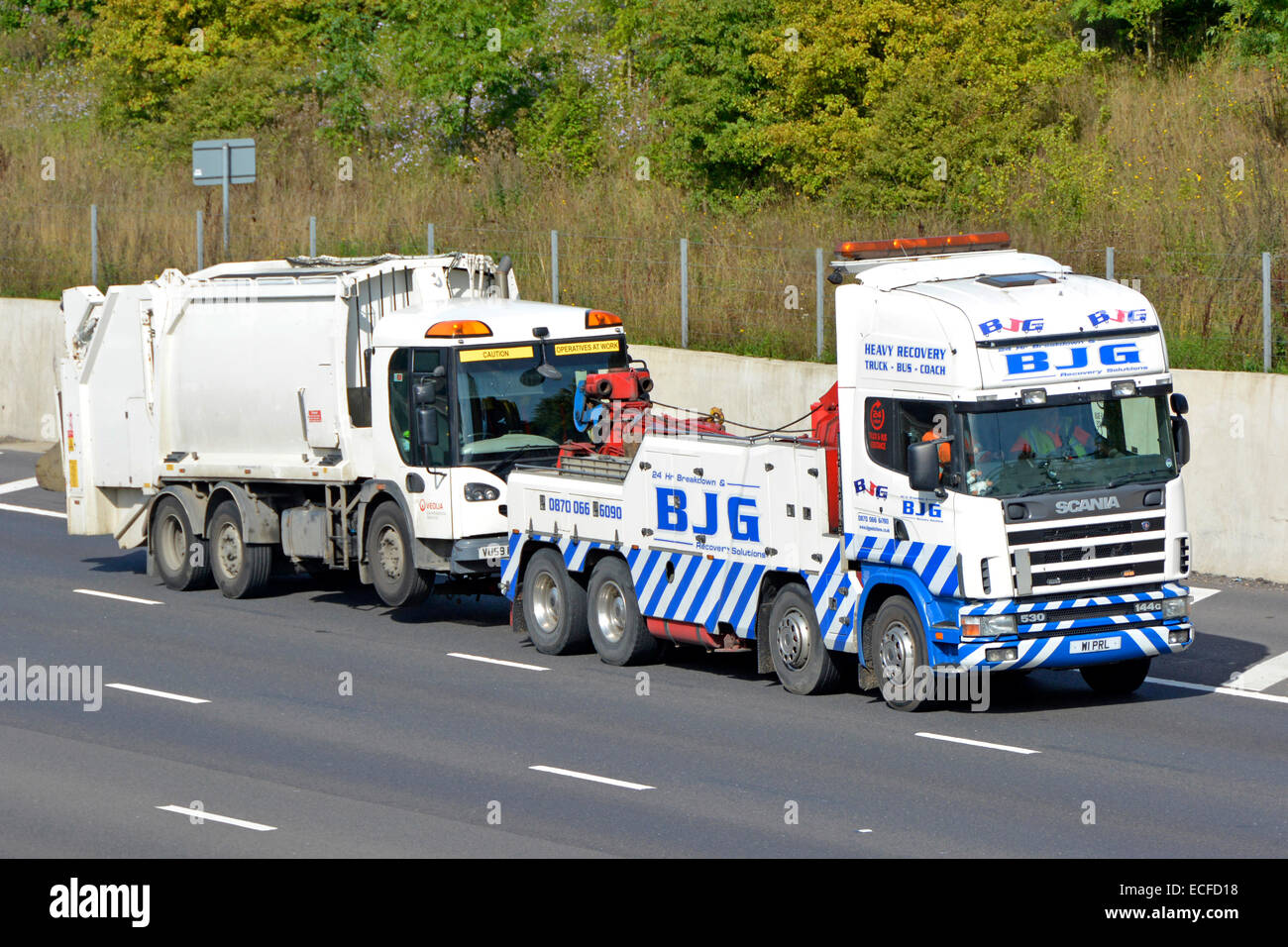 Heavy hgv Scania breakdown rescue tow truck moving a white Veolia garbage rubbish refuse dustcart bin lorry truck off of m25 motorway road England UK Stock Photo