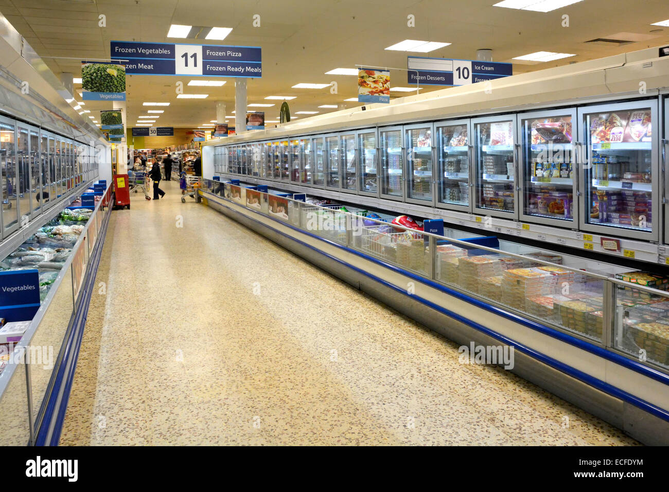 Shoppers & interior view Tesco supermarket frozen food aisle and cold cabinets shopping inside with terrazzo floor interior East London England UK Stock Photo