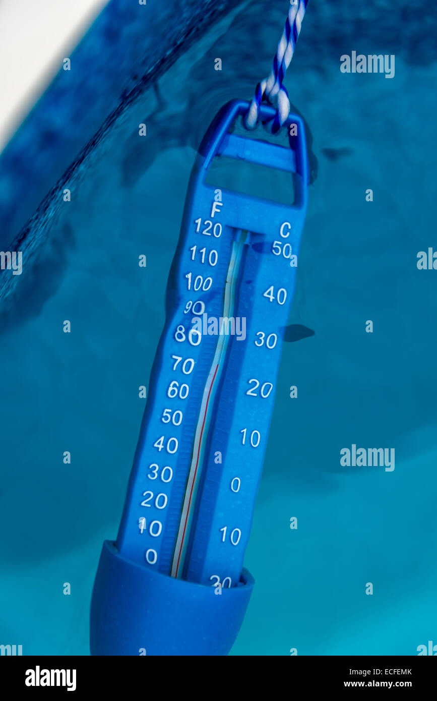 A blue pool thermometer partially submerge in the pool water. Stock Photo