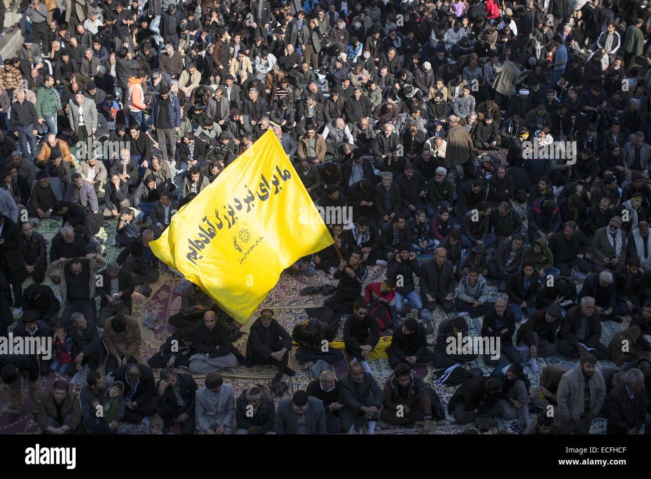 Tehran, Iran. 13th Dec, 2014. December 13, 2014 - Tehran, Iran - A Shi'ite Muslim man waves a yellow flag with a Persian script reads, We are ready for the battle, as he sit in a holy shrine during a ceremony to mark the religious ritual of Arbain in Shahr-e-Rey in south of Tehran. Morteza Nikoubazl/ZUMAPRESS © Morteza Nikoubazl/ZUMA Wire/Alamy Live News Stock Photo