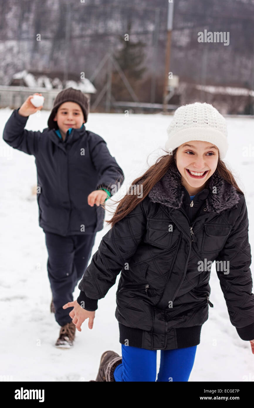 boy throw snow ball to the running girl. Children playing together outside in winter season Stock Photo