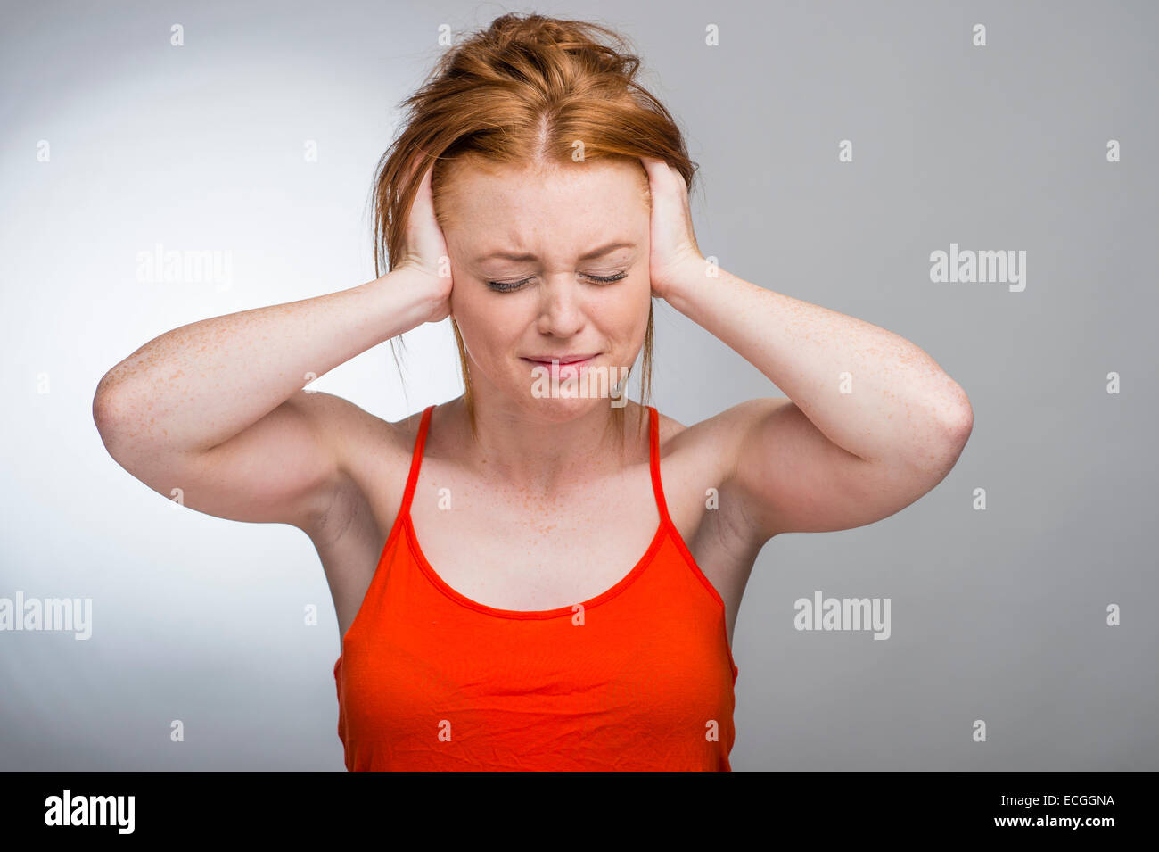 A ginger haired freckled skinned 16 17 18 year old slim caucasian teenage british girl with her hands over her ears UK Stock Photo