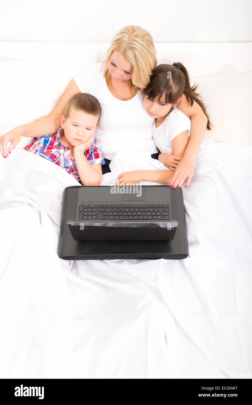 A mother using with her son and daughter a laptop computer in bed Stock