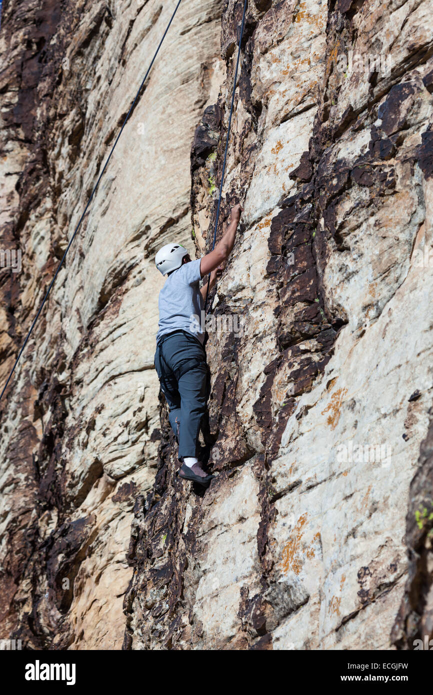 young man climbing a sandstone cliff with all the necessary safety gear ...