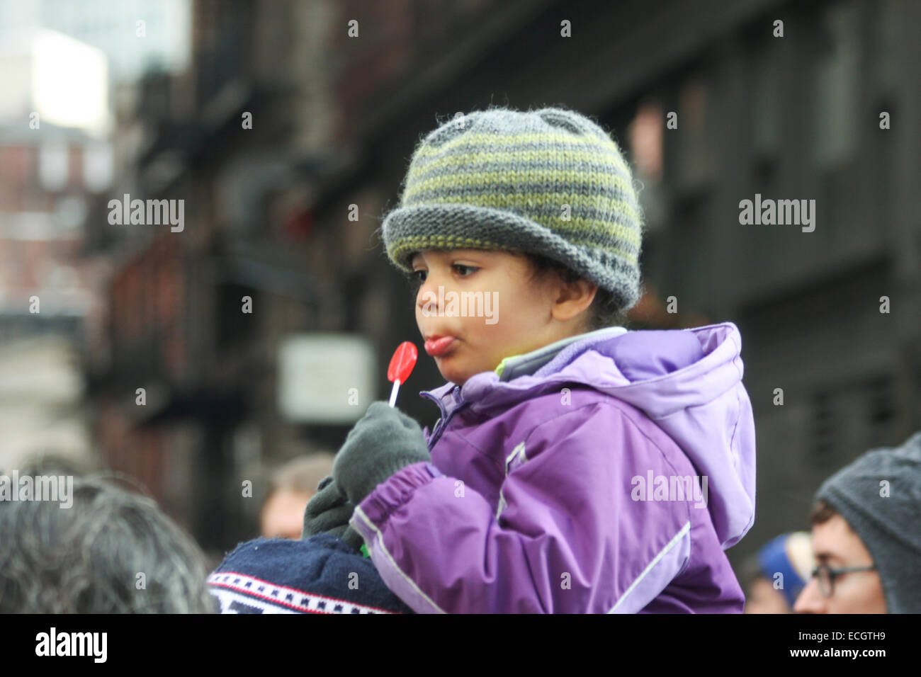 Boston, Massachusetts, USA. 13th December, 2014. A small child with a lollipop sits on an adult's shoulders during the Millions March rally in Boston, Massachusetts, USA.  The protest, like those in other cities throughout the United States on this day, is in response to recent grand jury verdicts not indicting the police officers who  killed unarmed black men Michael Brown and Eric Garner, and to the longstanding problems of racism and police brutality. Credit:  Susan Pease/Alamy Live News Stock Photo