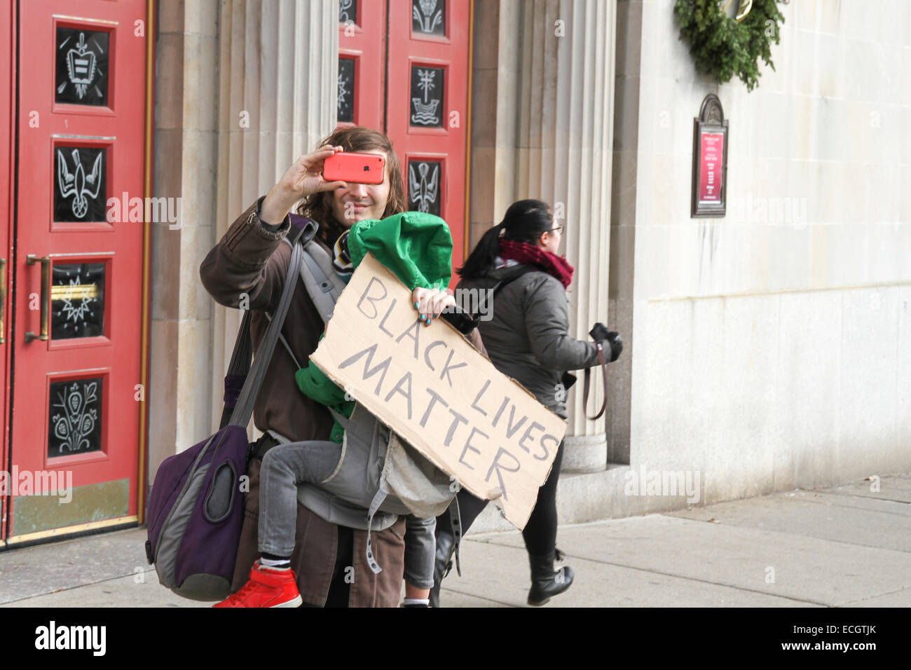 Boston, Massachusetts, USA. 13th December, 2014. An adult holding a child and 'Black Lives Matter' sign photographs marchers at the Millions March rally in Boston, Massachusetts, USA.  The protest, like those in other cities throughout the United States on this day, is in response to recent grand jury verdicts not indicting the police officers who  killed unarmed black men Michael Brown and Eric Garner, and to the longstanding problems of racism and police brutality. Credit:  Susan Pease/Alamy Live News Stock Photo