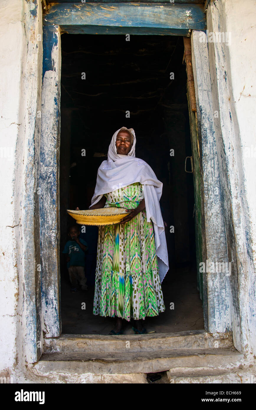 Friendly old woman standing with a basket of corn in a door frame, near Keren, Eritrea Stock Photo