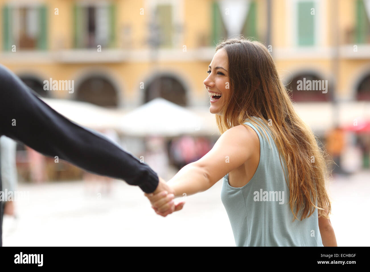 Happy tourist woman laughing and pulling her boyfriend in a touristic place Stock Photo