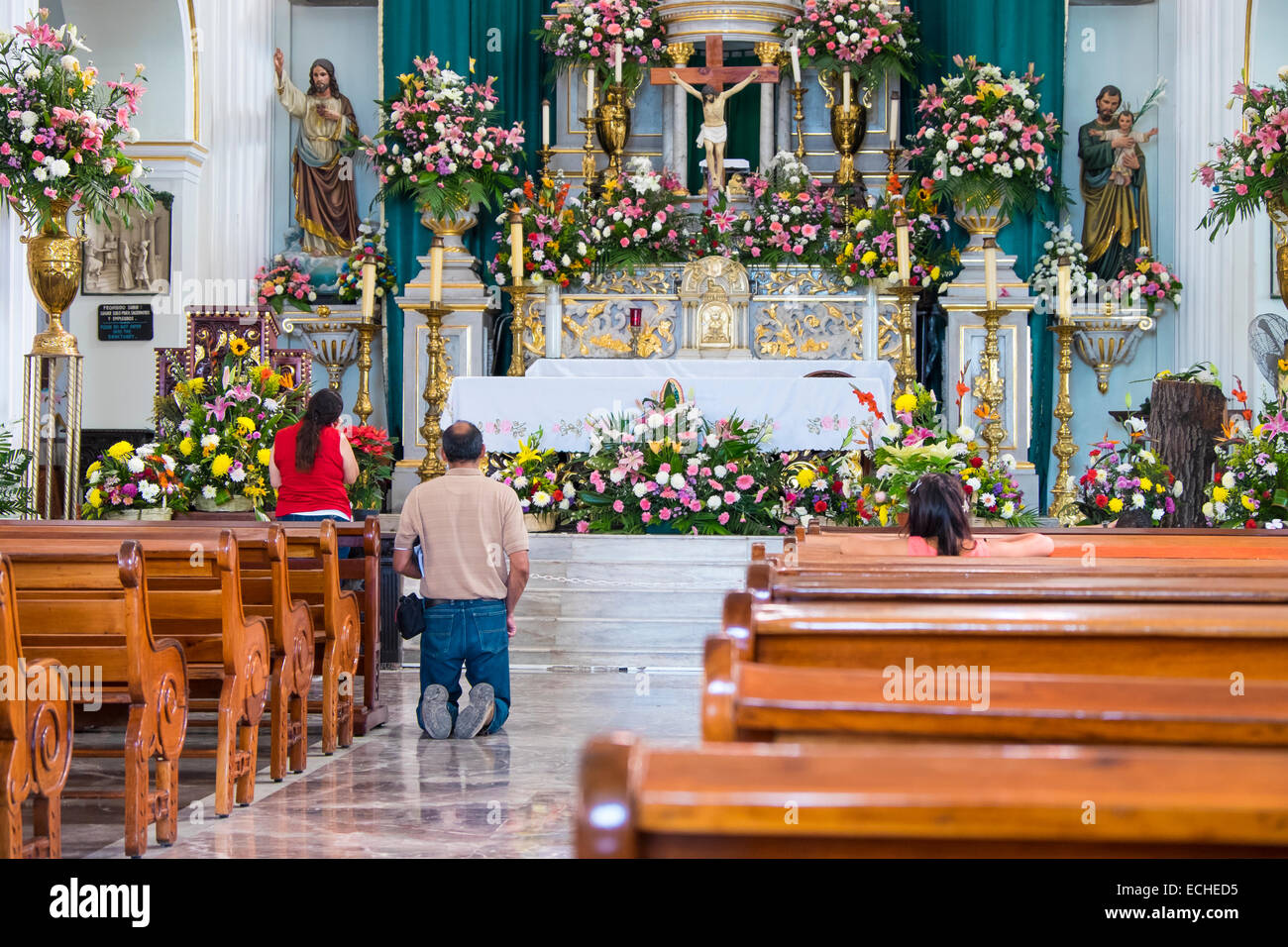 Mexican people praying in a church in Puerto Vallarta, Mexico. A man is approaching the altar and saying a prayer on his knees. Stock Photo