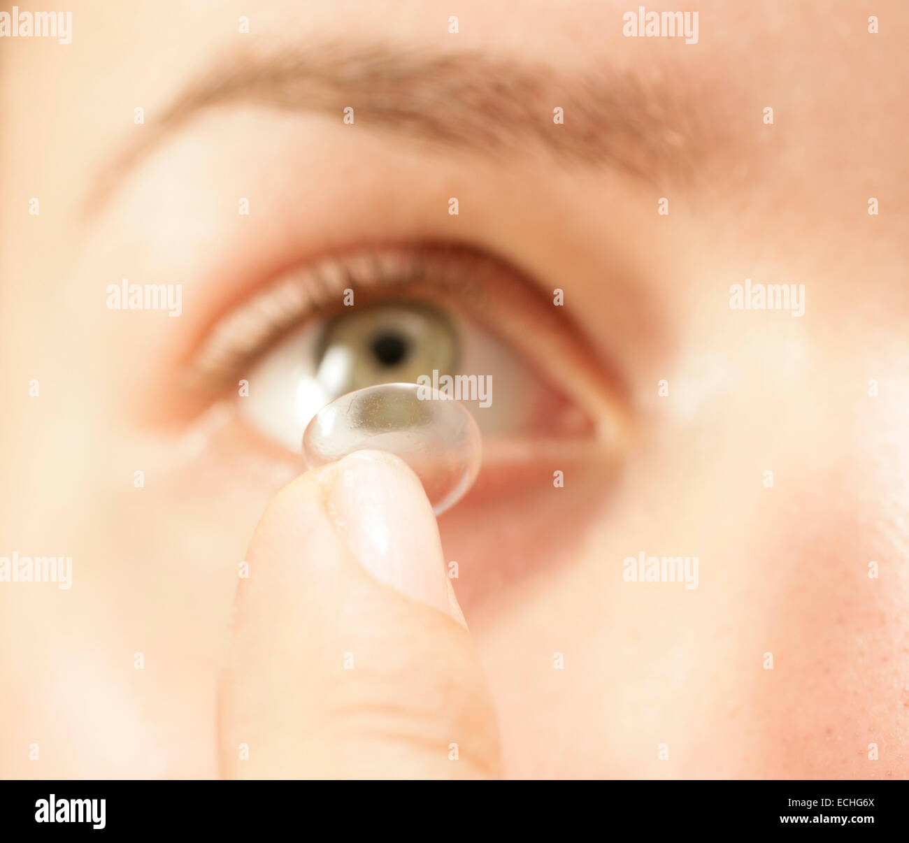 A close up straight on shot of a female putting in a contact lens into her eye Stock Photo