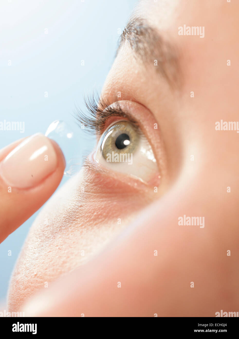 A close up at an angle of a female putting in a contact lens into her eye Stock Photo