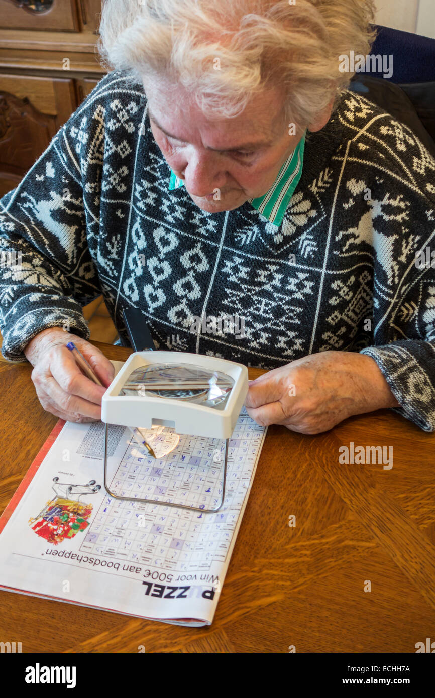 Elderly woman suffering from presbyopia / myopia / short-sightedness looking at crossword puzzle through magnifying glass Stock Photo