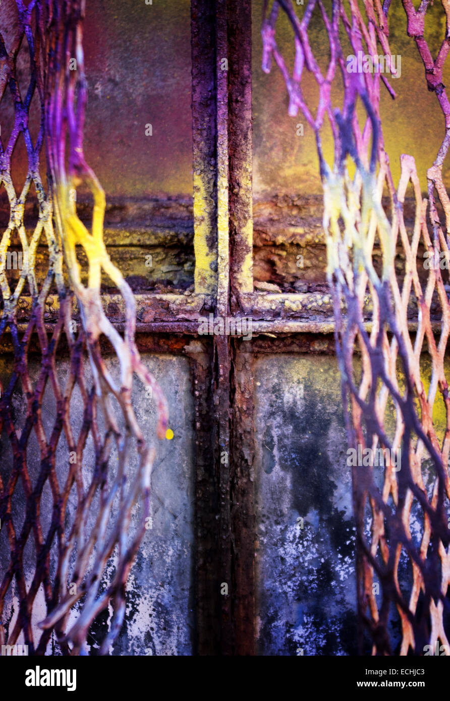 Abstract of a dilapidated window behind torn wire mesh, with traces of purple and yellow paint. Stock Photo
