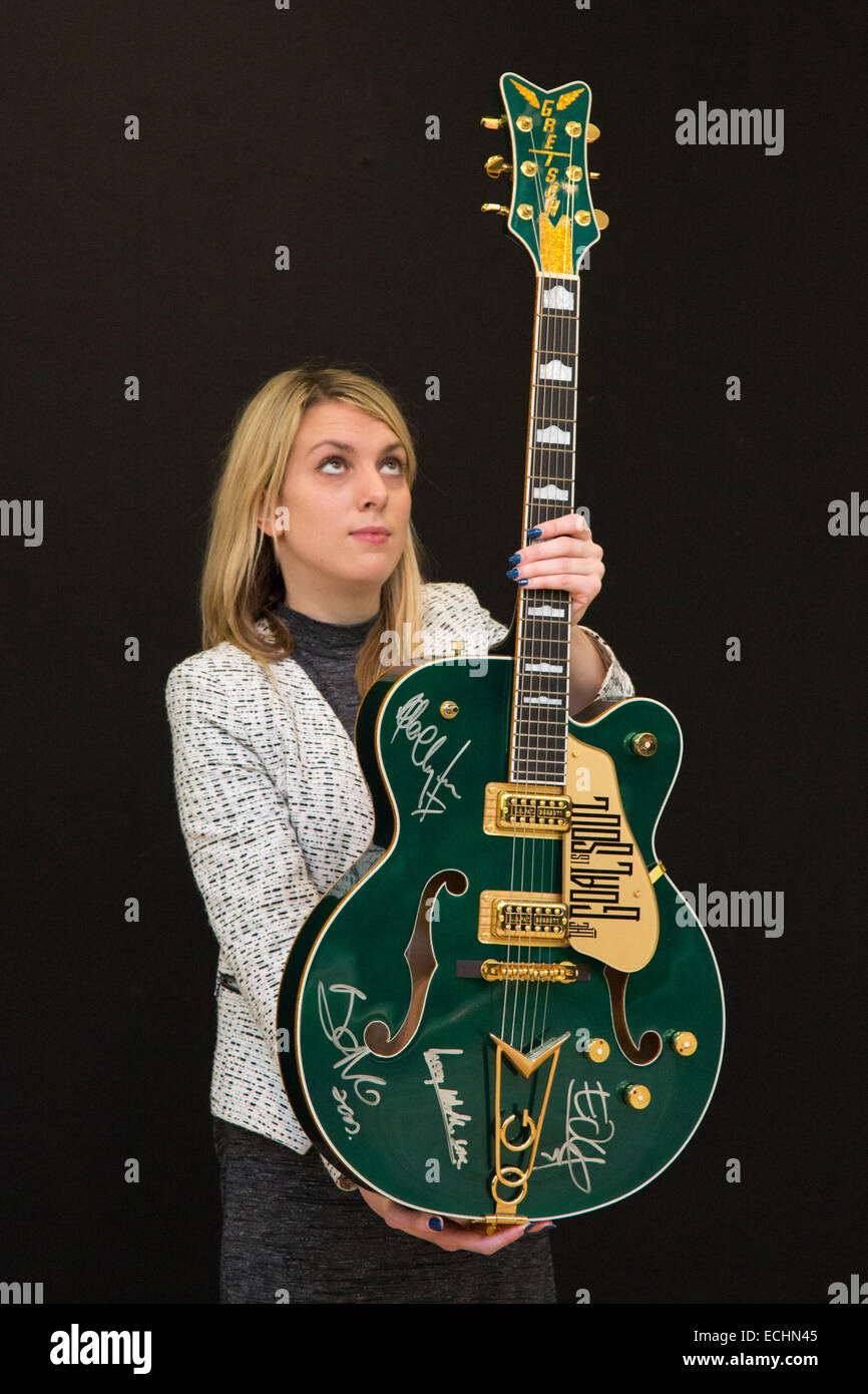 London, UK. 12 December 2014. A Christie's employee poses with Bono's custom prototype Gretsch Irish Falcon electric guitar signed by all four members of U2, estimate GBP 120,000-180,000. Christie's unveils Memorabilia of Hollywood Icons & Music Legends from the 20/21 Pop Culture Sale ahead of a free public view from 13 to 16 December 2014, with the auction taking place on 16 December. The sale celebrates some of the great names of 20th century cinema and music legends, featuring costumes and film scripts, instruments and handwritten song lyrics. Stock Photo