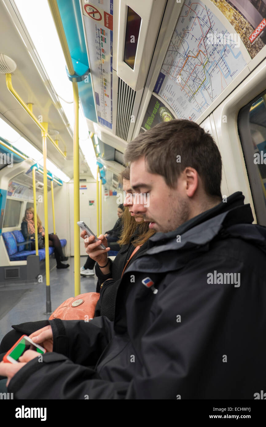 Man playing game on a mobile phone whilst commuting on a London Underground train Stock Photo