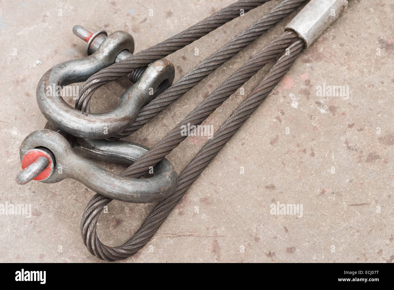 Two used steel wire loops on a concrete floor with one shackle through each. Stock Photo
