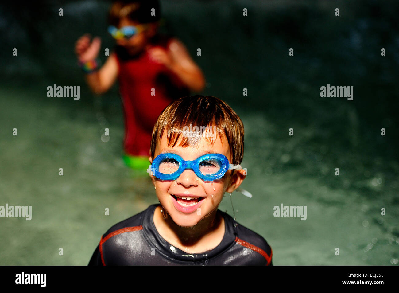 A young boy wearing goggles smiles while in a swimming pool Stock Photo