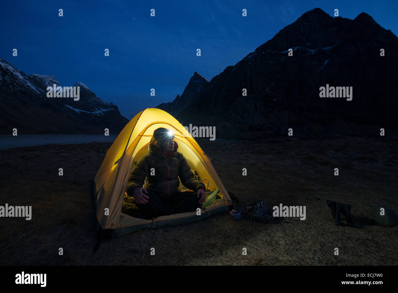 Female hiker sits in tent illuminated at night while wild camping at scenic Horseid beach, Moskenesøy, Lofoten Islands, Norway Stock Photo
