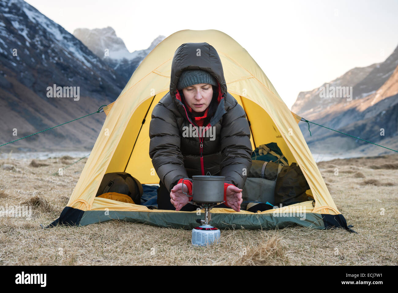 female hiker warms hands with stove on cold morning wild camping at Horseid beach, Moskenesøy, Lofoten Islands, Norway Stock Photo