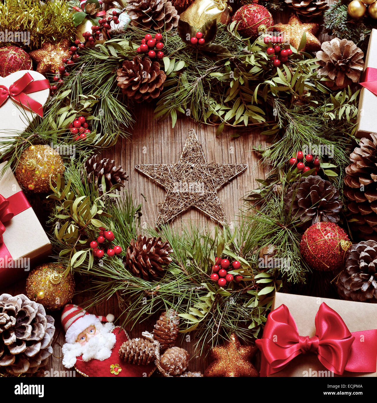 a rustic wooden table full of gifts, and christmas ornaments, such as a natural wreath with branches, berries and pine cones, or Stock Photo
