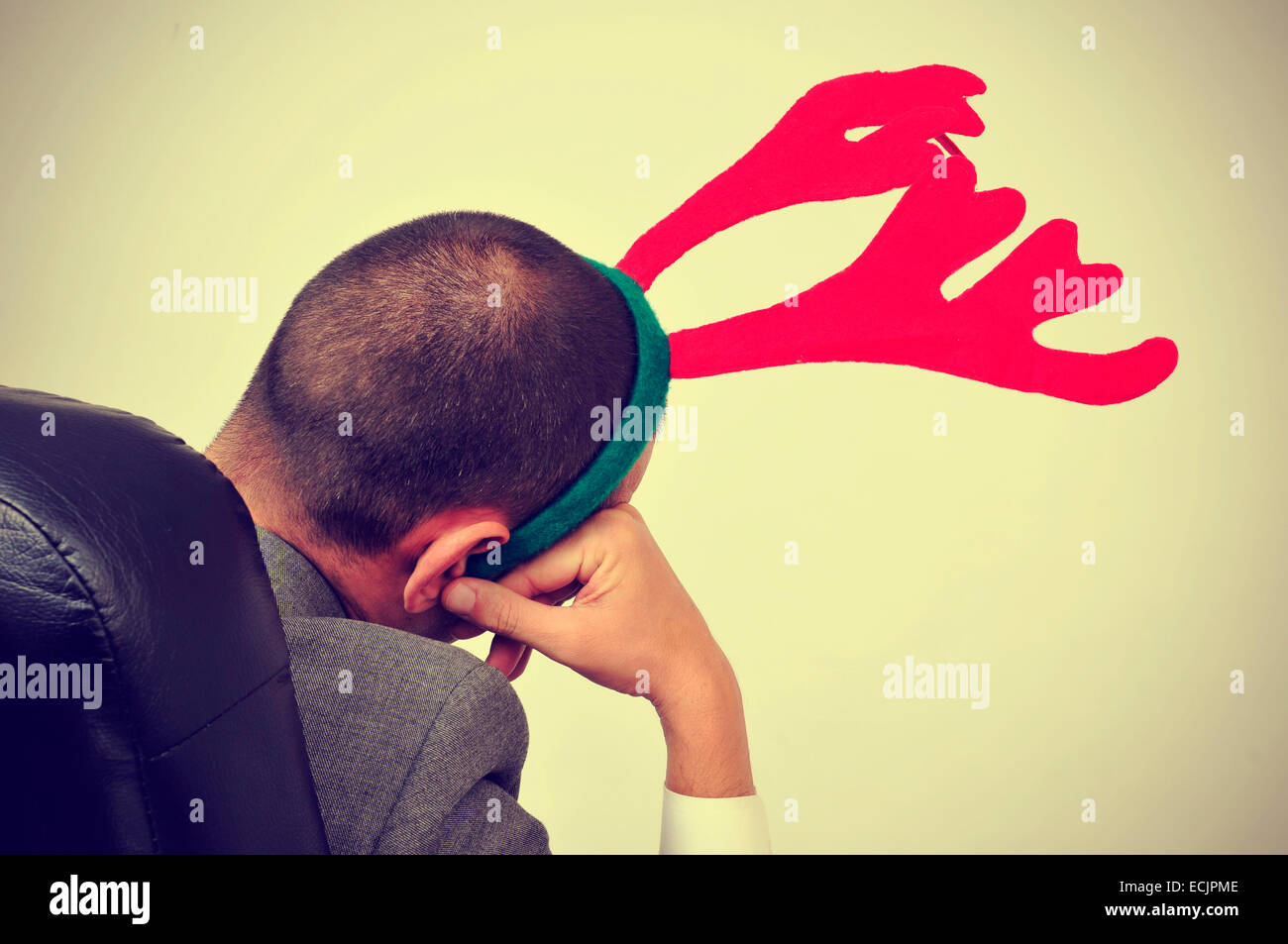 a man with a reindeer antlers headband relaxing in his office chair after an office christmas party, with a filter effect Stock Photo