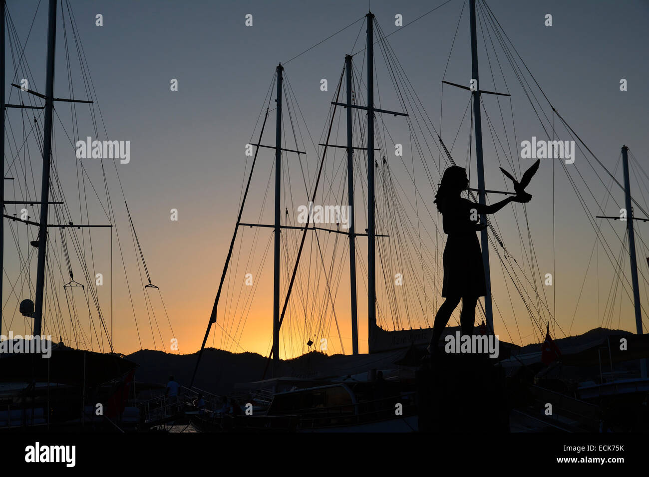 Statue of a girl with dove, at sunset, in Marmaris, Turkey, with yacht masts against the sky Stock Photo