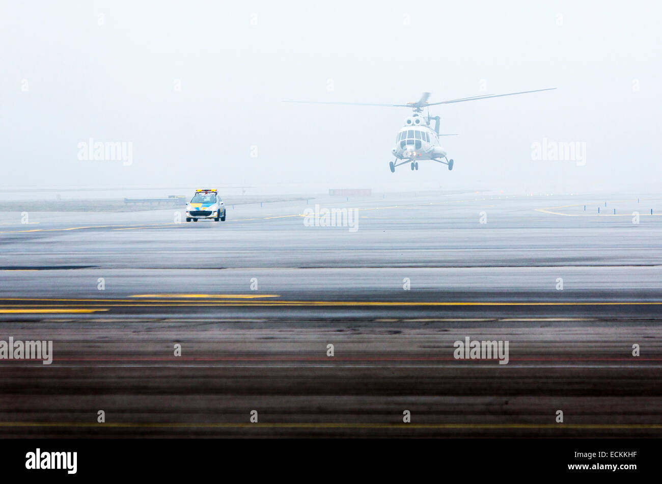 Helicopter on a foggy landing strip led by a car. Stock Photo