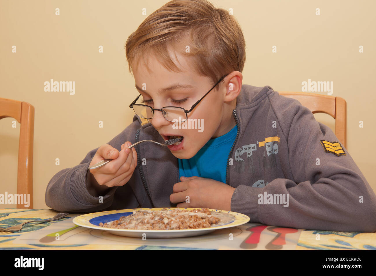 A small boy is eating his meal sitting at the table. Stock Photo