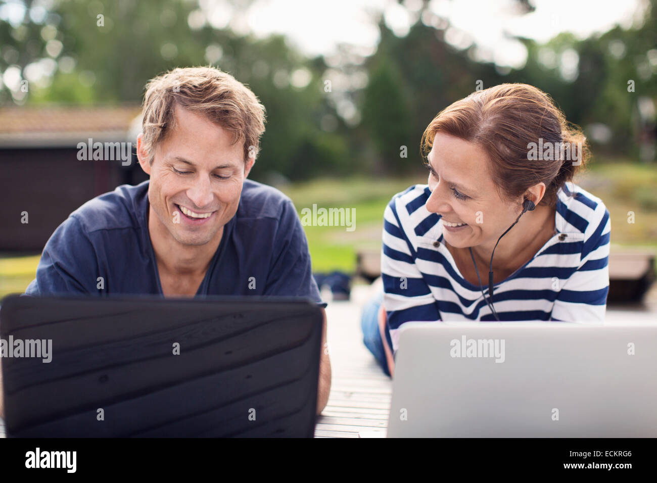 Smiling mature couple using laptops while lying on pier Stock Photo