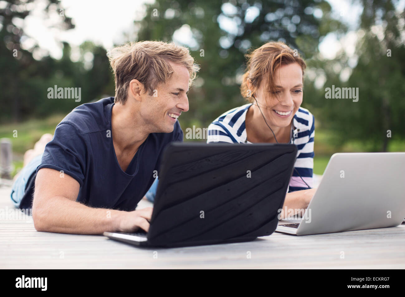 Happy mature couple using laptops while lying on pier Stock Photo