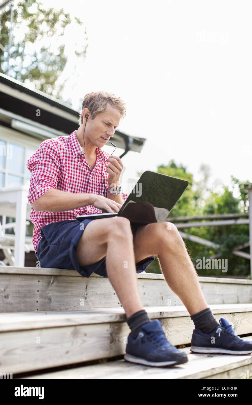 Man using handsfree device and laptop while sitting on porch against