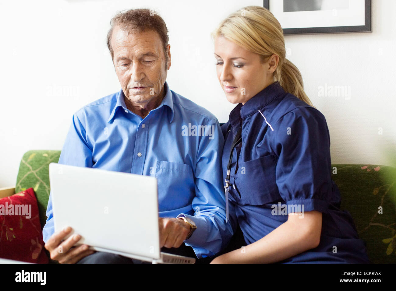 Female caretaker and senior man using laptop at nursing home Stock