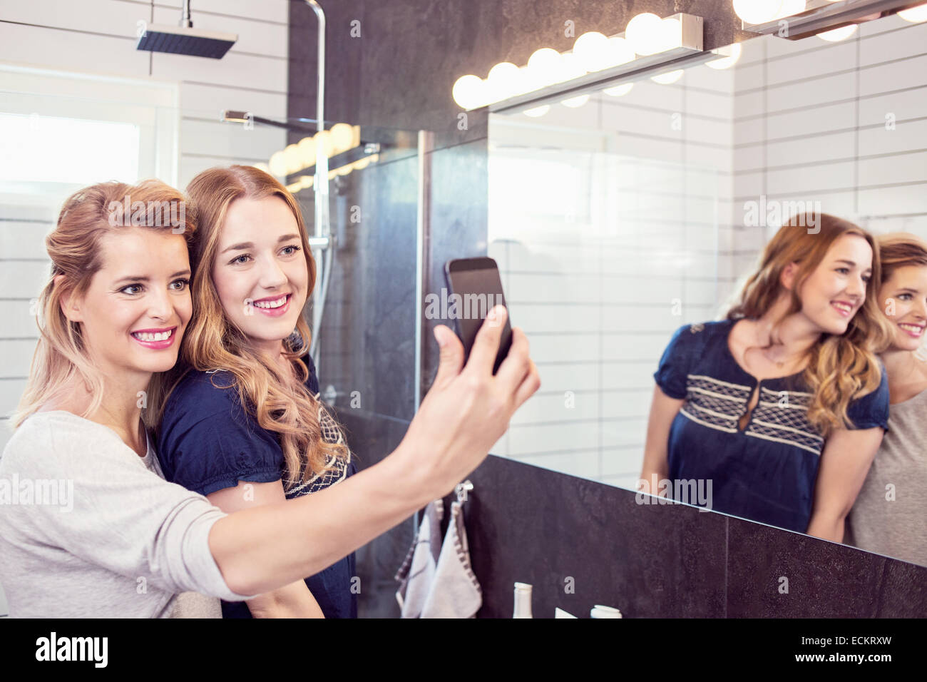Happy female friends taking self-portrait with cell phone in bathroom Stock Photo