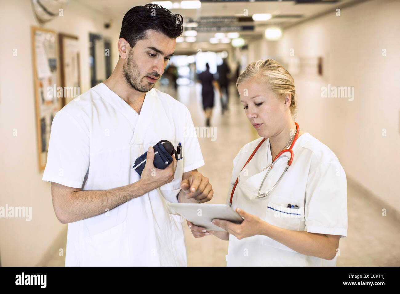 Male and female doctors discussing over digital tablet in hospital corridor Stock Photo