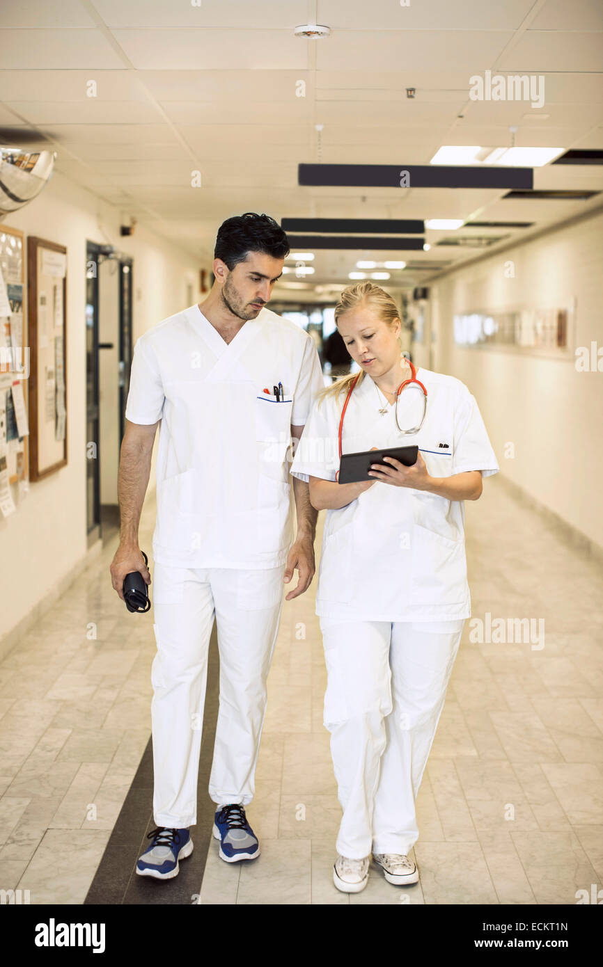 Full length of doctors discussing over digital tablet in hospital corridor Stock Photo