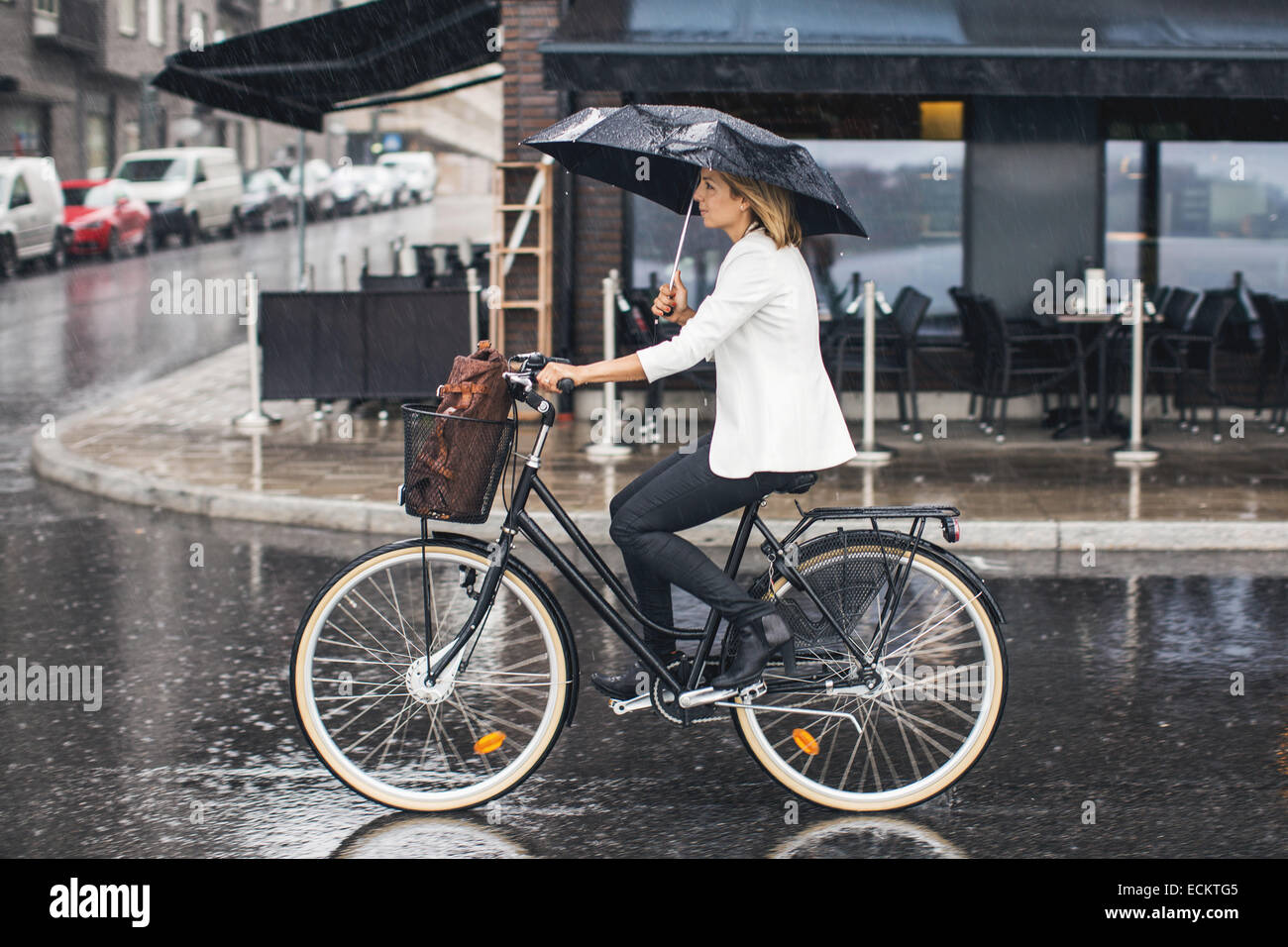 Businesswoman riding bicycle on wet city street during rainy season Stock Photo