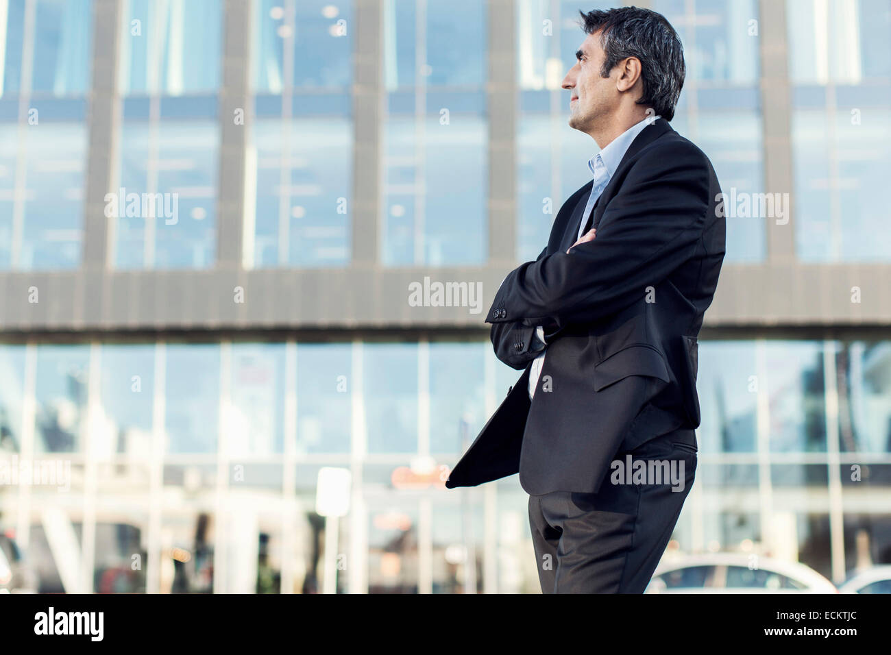 Businessman with arms crossed looking away outside office building ...