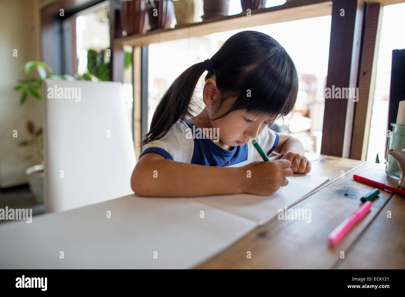 Girl with pigtails sitting at a table, drawing with felt tip pens. Stock Photo
