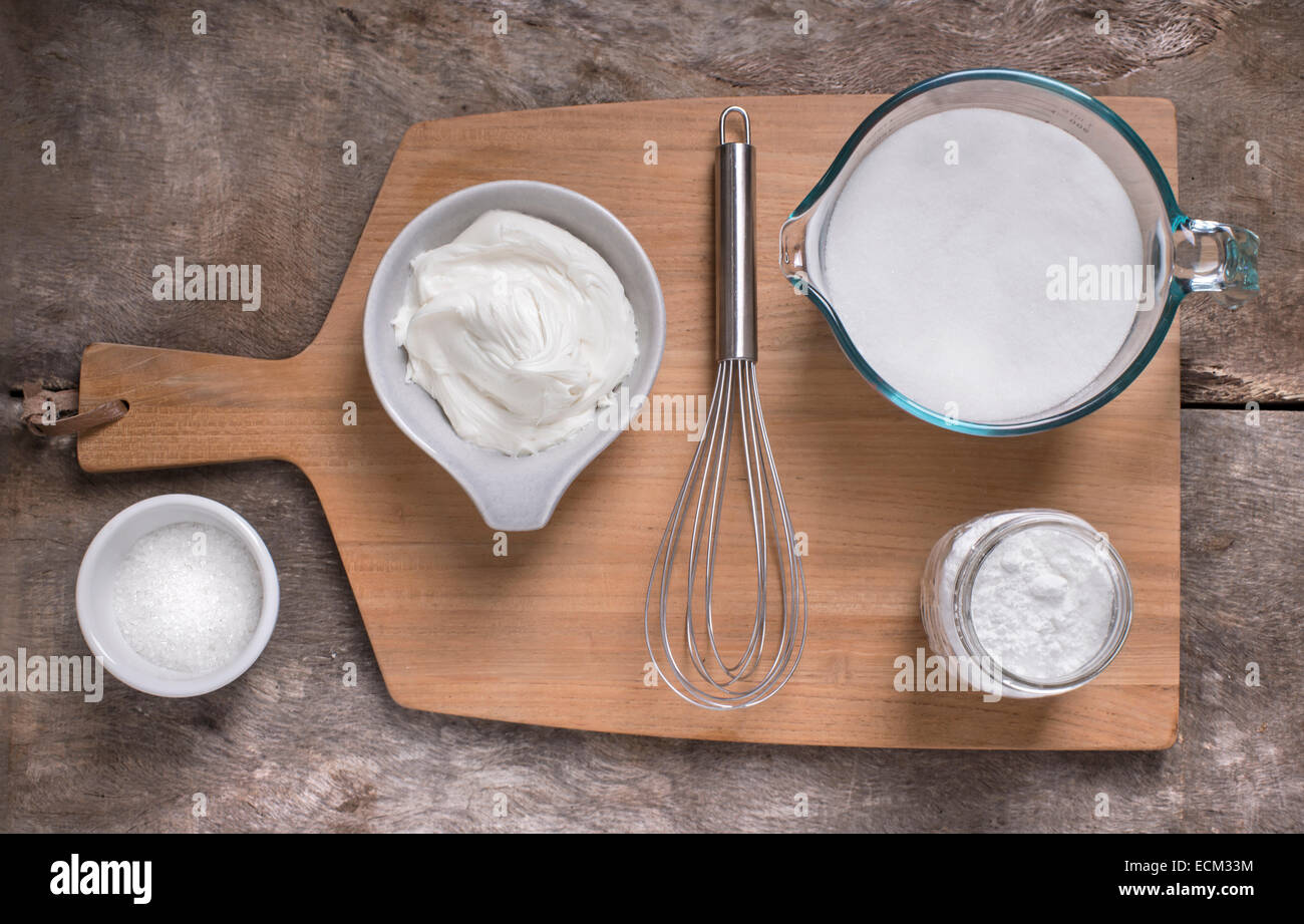 Top down view of white frosting and ingredients on light cutting board and light rustic wood surface. Light and clean. Stock Photo