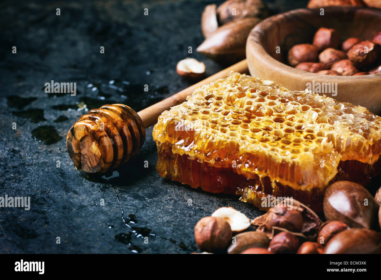 Honeycomb with honey dipper and mix of nuts over black surface. Stock Photo
