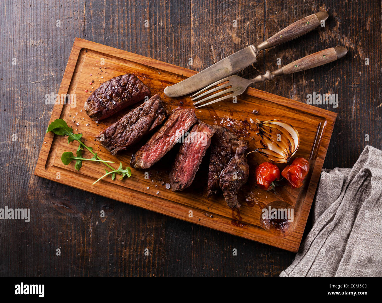 Sliced medium rare grilled Beef steak Ribeye with grilled onions and cherry tomatoes on cutting board on wooden background Stock Photo