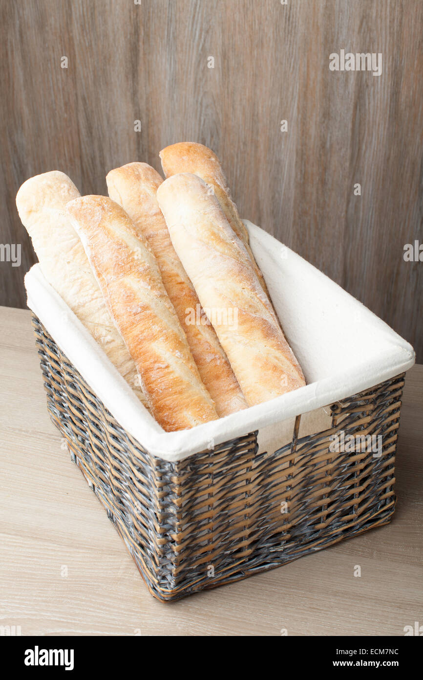 Stack of traditional fresh-baked French bread loafs baguette served in woven basket on wooden background Stock Photo