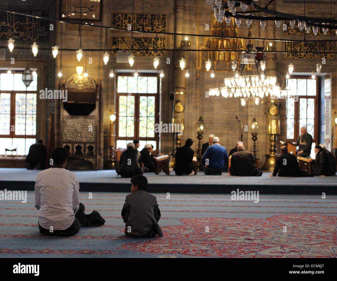 Boy watching his father while praying in Yeni Cami (New Mosque), Eminonu, Istanbul. People are praying in background. Stock Photo